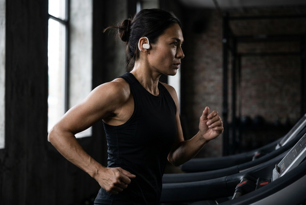 Female athlete running on a treadmill wearing white Open Ear Air Pro