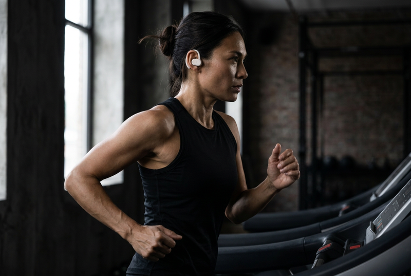 Female athlete running on a treadmill wearing white Open Ear Air Pro